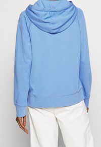 Felpa blu chiaro realizzata in tessuto morbido con una vestibilità rilassata, con un grande cappuccio, polsini e orlo a coste, e dettagli di cucitura visibili.