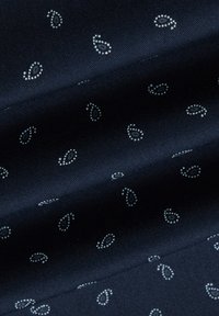 Granatowa tkanina o gładkiej fakturze zdobiona małymi białymi wzorami paisley równomiernie rozmieszczonymi na całej powierzchni.