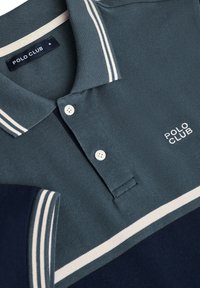 Mörk teal pikétröja med vita ränder på kragen och ärmarna, med en treknappsslutning och "POLO CLUB"-logotyp i vitt.
