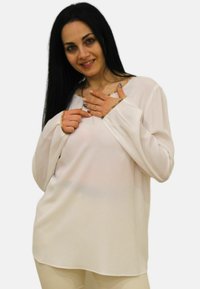 Blusa bianca a maniche lunghe con vestibilità ampia e scollatura rotonda. Tessuto morbido e liscio con un leggero lucido e rifiniture dorate sui polsini.