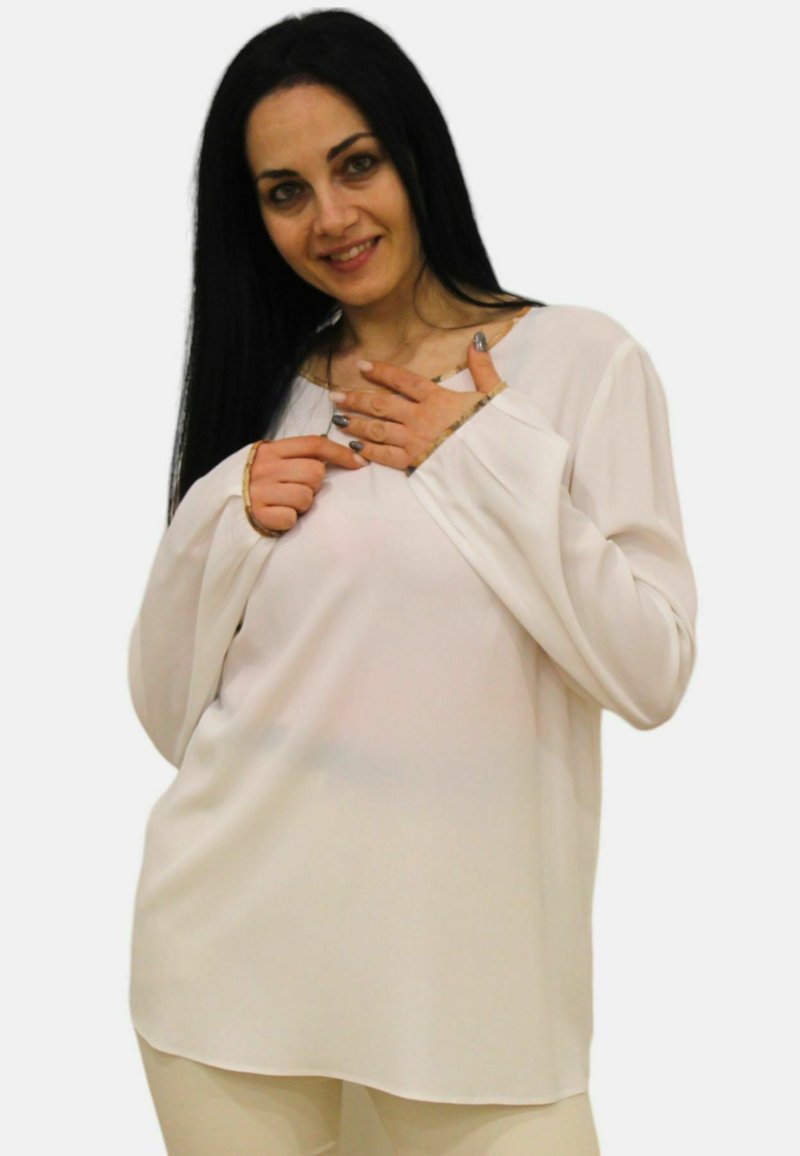 Blusa bianca a maniche lunghe con vestibilità ampia e scollatura rotonda. Tessuto morbido e liscio con un leggero lucido e rifiniture dorate sui polsini.