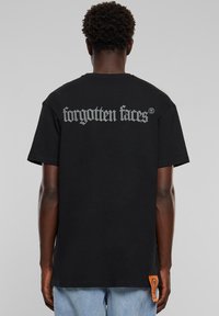 Black cotton t-shirt featuring silver "forgotten faces" text on the back. Includes a small orange label at the side. Regular fit.