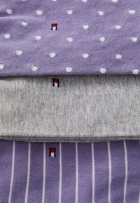 Tris sulankstytų kojinių: viršutinė šviesiai violetinė su baltais taškeliais, vidurinė pilka, apatinė šviesiai violetinė su vertikaliomis juostomis, kiekviena su logotipo detale.