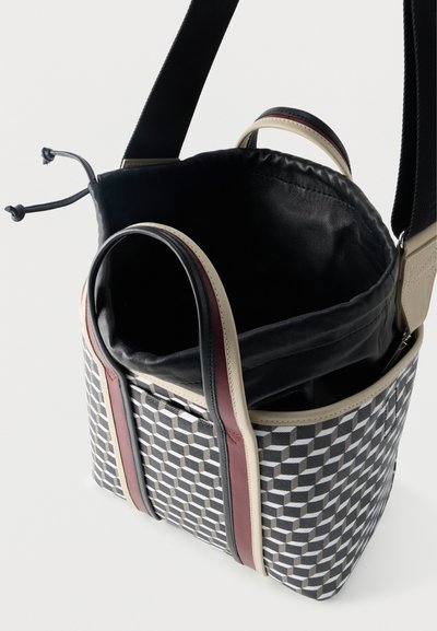 Άνοιχτη τσάντα tote με ασπρόμαυρο γεωμετρικό μοτίβο, δερμάτινη επένδυση, διπλές λαβές και πλατιά μαύρη ιμάντα ώμου σε λευκό φόντο.