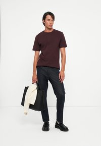 Tricou scurt de culoare burgundă, blugi dark denim și pantofi din piele negri. Poartă o geantă tote neagră cu un pulover crem așezat peste ea.