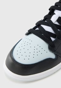 Czarny skórzany sneaker z jasnoniebieską perforowaną częścią na przodzie, czarnymi sznurowadłami, białym środkiem podeszwy i fakturowaną podeszwą zapewniającą przyczepność.