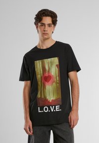 Melna kokvilnas T-kreklā centrā ir grafika ar sarkanu sirdi zaļā mežā, zem tās ir drukāti vārdi "L.O.V.E." treknrakstā baltās krāsas.
