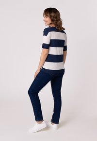 Chemise à rayures bleu marine et gris clair à manches courtes avec des poignets retroussés, associée à un jean ajusté bleu foncé et des baskets blanches.