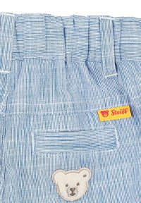 Gestreifte blaue Baumwollshorts mit einem strukturierten Bärenpatch und einem kleinen gelben Steiff-Label, das am Bund angenäht ist.