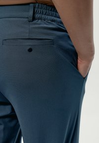 Námornícke modré nohavice vyrobené z textilného materiálu, s elastickým pásom, bočnými vreckami a jedným zadným vreckom s detailom na gombíku.