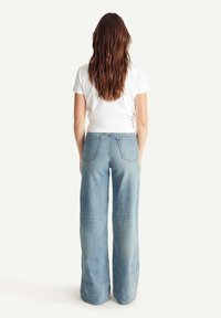 Vaqueros de pierna ancha de mezclilla azul, con una cintura alta y dos bolsillos traseros, combinados con una camiseta blanca ajustada.