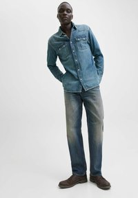 Cămașă din denim de culoare albastră deschisă, având două buzunare la piept și închidere cu nasturi. Asortată cu blugi decolorati de culoare albastră și pantofi maro închis.