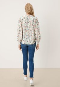 Blusa a maniche lunghe in tessuto leggero con motivo floreale in colori pastello, dotata di una schiena arricciata e colletto con bottoni.