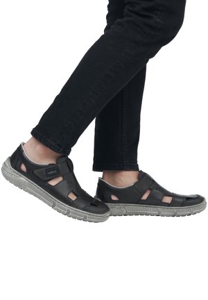 Schwarze Sandale mit offenen Ausschnitten, aus synthetischem Material, mit gepolsterter Sohle und verstellbarem Riemen. Eignet sich für legere Anlässe und warmes Wetter.