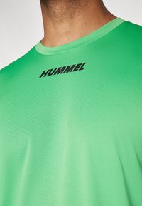 Roheline spordipait, mis on valmistatud tekstureeritud kangast, millel on ümar kaelus ja must "HUMMEL" logo. Kujundus on lihtne, ilma mustrite või aksessuurideta.