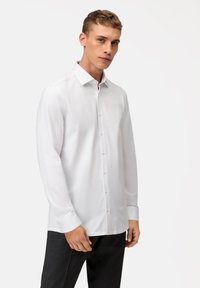 Chemise blanche à manches longues en tissu lisse, dotée d'un col classique et d'une fermeture à boutons sur le devant avec des boutons de couleur claire.