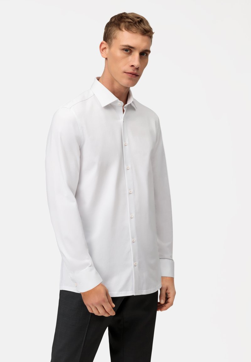 Chemise blanche à manches longues en tissu lisse, dotée d'un col classique et d'une fermeture à boutons sur le devant avec des boutons de couleur claire.