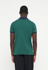 Zelená polokošeľa s námorníckym golierom a akcentmi na rukávoch, krátke rukávy a hladká bavlnená textúra. Viditeľné švy na leme.