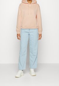 Roze hoodie met een voorzak en een trekkoord, gecombineerd met lichtblauwe rechte jeans en witte sneakers. Casual outfit.