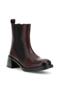 Botină Chelsea din piele maro închis cu panou elastic lateral negru, toc bloc, vârf rotunjit și cârlig la spate.