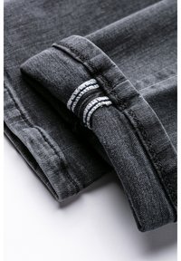 Šedá džínová tkanina složená s manžetou, která ukazuje kontrastní bílé šití. Textura působí měkce, ale pevně, zdůrazňující neformální design.