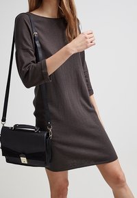 Robe longue à manches longues, couleur marron foncé, avec un décolleté bateau, associée à un sac à main noir au design épuré et aux accessoires métalliques.