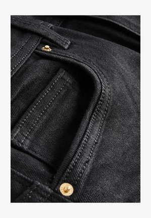 Primo piano di una tasca di jeans in denim nero con cuciture visibili e due piccoli rivetti in ottone vicino al bordo della tasca.