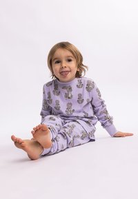 Purple pajama set featuring cartoon bunnies, made of soft fabric, with long sleeves and an elastic waist. Child sitting barefoot, smiling.