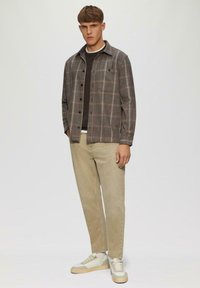 Graham-karierte Button-up-Hemd mit einem schwarzen Rundhalsausschnitt darunter, kombiniert mit hellbeigen Hosen und beigen Sneakers, bestehend aus einem lässigen Schnitt und Taschen.