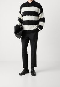 Sweter w czarno-białe paski o puszystej fakturze, do tego czarne, dopasowane spodnie i czarne buty, trzymając czarną torbę typu tote.