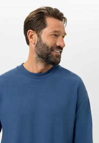 Blaues Sweatshirt mit Rundhalsausschnitt aus weichem Stoff, mit geripptem Kragen und entspanntem Schnitt, langen Ärmeln und minimalen Details.