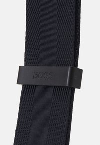 Cintura elastica blu navy con motivo testurizzato e una fibbia nera opaca con il nome del marchio "BOSS" in rilievo. Design minimalista e materiale resistente.