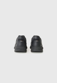 Adidași atletici negri cu un superior din piele netedă, accente texturate, panouri din plasă și o talpă din cauciuc negru căptușită.