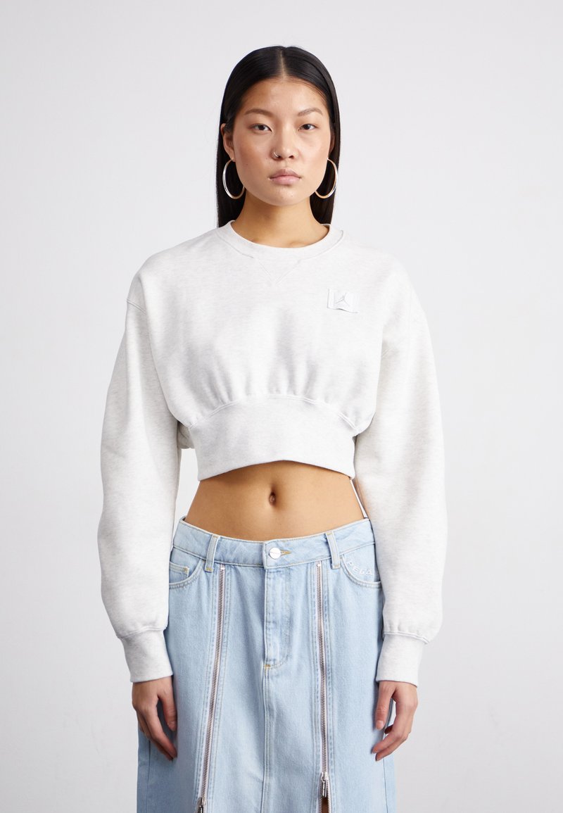 Lys grå kort sweatshirt med lange ermer og ribbet kant, med en liten logo-patch på brystet. Kombinert med et lys blått denimskjørt.