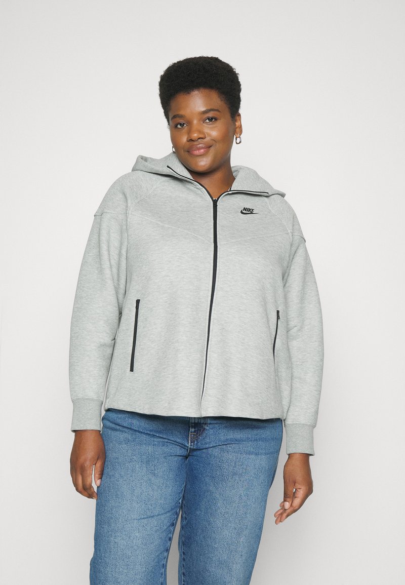 Sweat à capuche zippé gris en tissu doux, avec des accents noirs et le logo Nike sur la poitrine. Poches sur les côtés avant.
