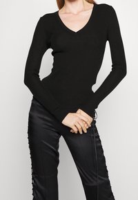 Černý žebrovaný top s dlouhým rukávem a výstřihem do V, přiléhavého střihu a plochými švy, doplněný lesklými černými kalhotami s bočním šněrováním.