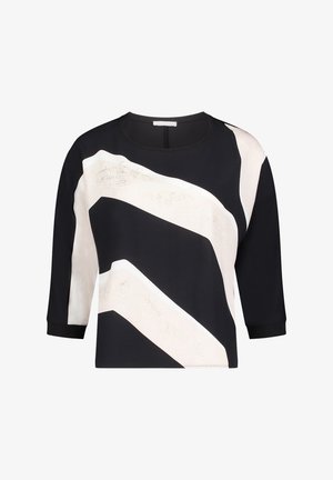 Haut court noir et crème à manches longues, présentant des motifs zigzag audacieux et une texture lisse. Encolure ronde avec bordure contrastante.