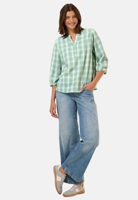 Camicia verde chiaro a quadri con vestibilità comoda, maniche a tre quarti e colletto. Abbinata a jeans a gamba larga blu e sneakers grigie.