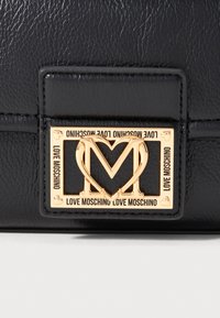 Black leather handbag featuring a gold metallic logo plaque with "LOVE MOSCHINO" text and heart detail, showcasing a textured surface.