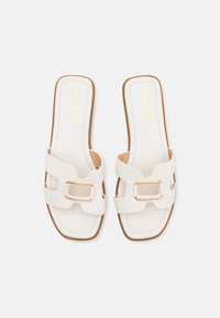 Vita slide-sandaler med två breda remmar, med en guldbuckle. Slät läderliknande material med platt sula och minimalistiska sömnadsdetaljer.