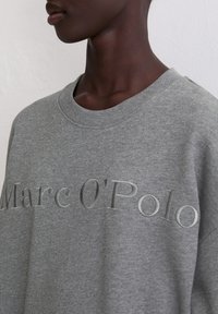 Szary sweatshirt z prążkowanym dekoltem, z wytłoczonym napisem "Marc O'Polo". Materiał wydaje się miękki, o gładkiej teksturze i luźnym kroju.