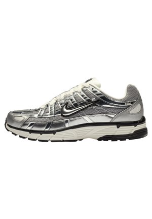 Chaussure de sport Nike argent et blanche avec logo swoosh noir, fermeture à lacets et semelle texturée, vue de profil sur fond blanc.