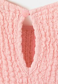 Gros plan sur un tissu rose texturé avec un décolleté en trou de serrure maintenu par un petit bouton rose en haut.