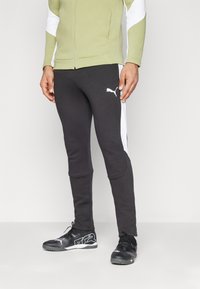 Pantaloni atletici negri cu panouri laterale albe, dintr-un material neted, cu o croială slim și manșete ribile la glezne. Asortați cu adidași negri cu accente albe.