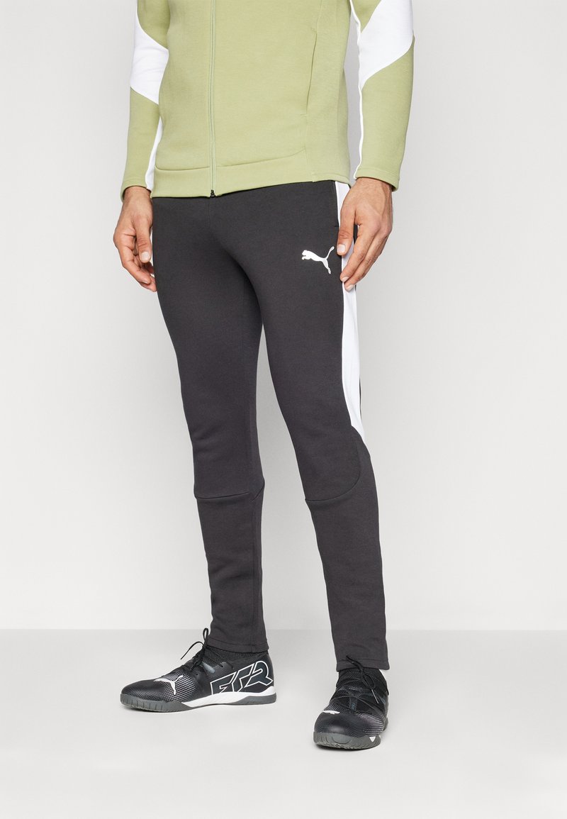 Pantaloni atletici negri cu panouri laterale albe, dintr-un material neted, cu o croială slim și manșete ribile la glezne. Asortați cu adidași negri cu accente albe.