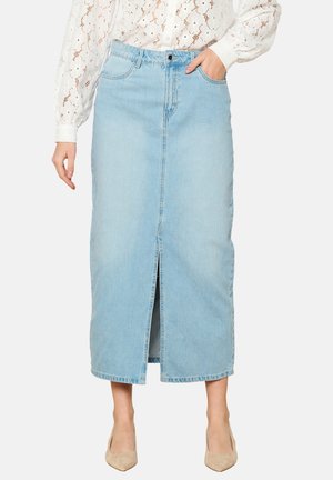 Gonna maxi in denim blu chiaro con spacco frontale, vita alta e design a cinque tasche. Abbinata a una blouse in pizzo bianco e tacchi nude.