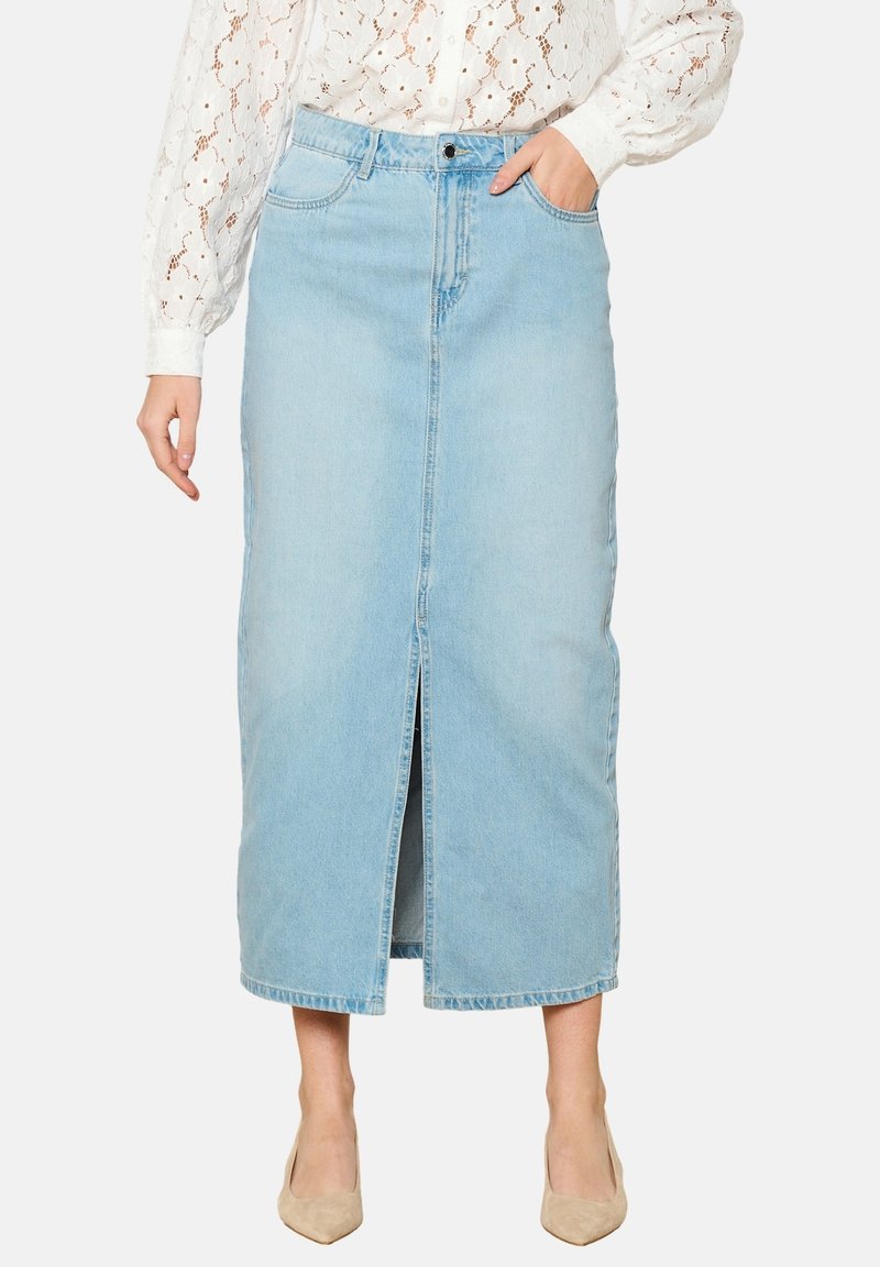 Denim maksi krilo v svetloblu z sprednjim razporkom, visokim pasom in petimi žepi. Slogirano z belim čipkastim bluzo in nude petami.