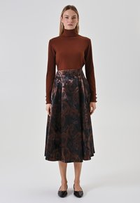 Brauner Rollkragenpullover kombiniert mit einem schwarzen, floral gemusterten, plissierten Rock. Der Rock verfügt über metallische Akzente und eine glatte Textur.