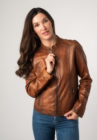 Bruine leren jas met een ritssluiting en geribbelde manchetten, voorzien van een staande kraag en twee zijzakken. Gladde textuur met natuurlijke glans.