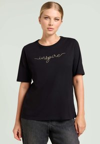 Camiseta negra de manga corta con cuello redondo y texto bordado en dorado que dice "inspire". La tela parece suave y ligera.